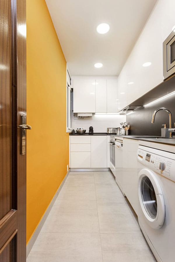 Cocina alargada con pared naranja y lavadora