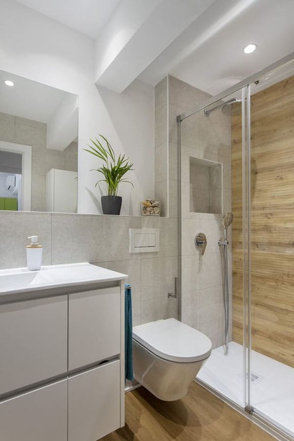 Baño reformado en blanco con mampara y pared con efecto madera