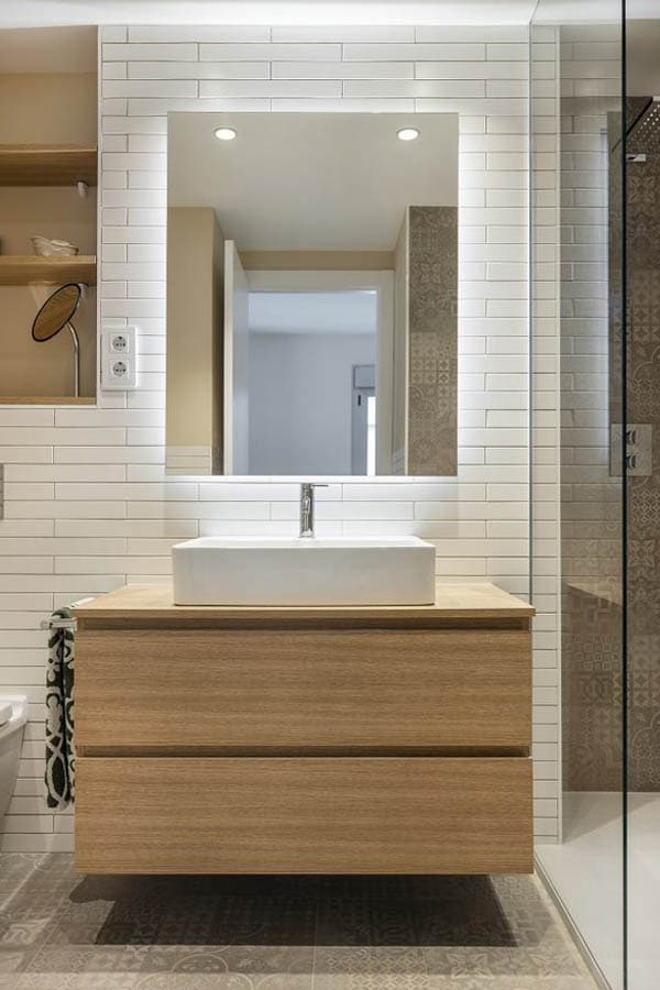Mueble de almacenamiento para baño en tono madera bajo un gran espejo