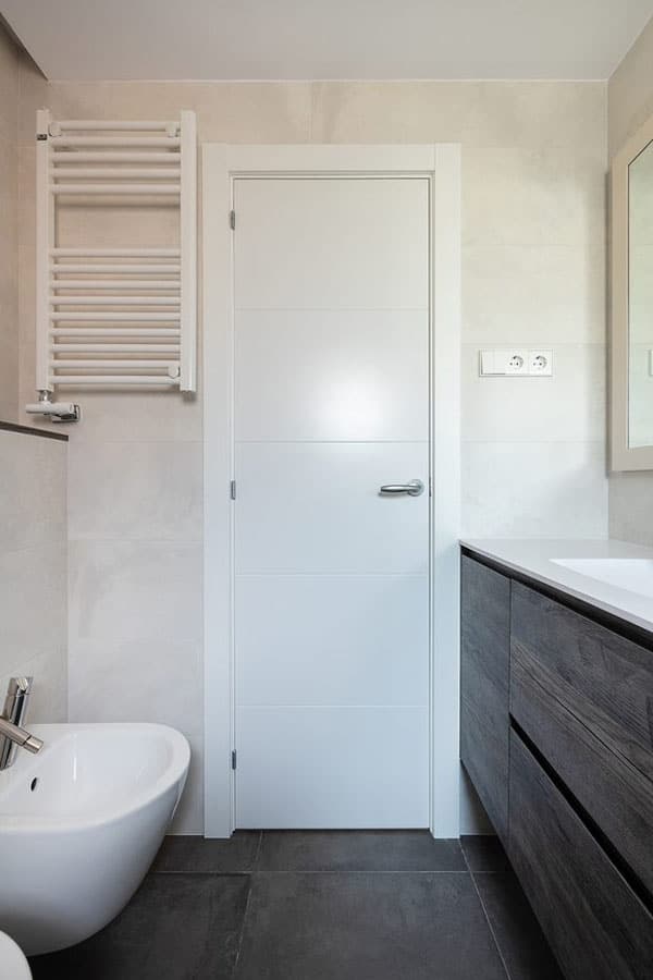 Puerta de baño blanca junto a un toallero eléctrico