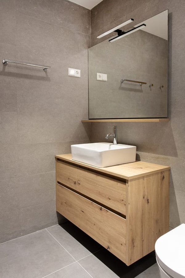 Baño con pequeño lavamanos en blanco sobre un mueble de almacenamiento con efecto madera