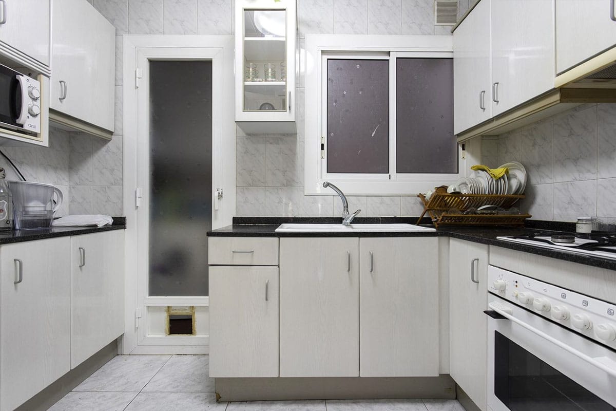 Cocina con mobiliario blanco y pequeña puerta hacia un lavadero