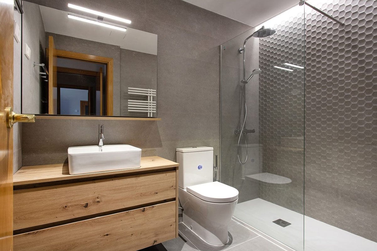 Baño reformado con mueble de almacenamiento bajo una pica sencilla, sanitario y mampara transparente